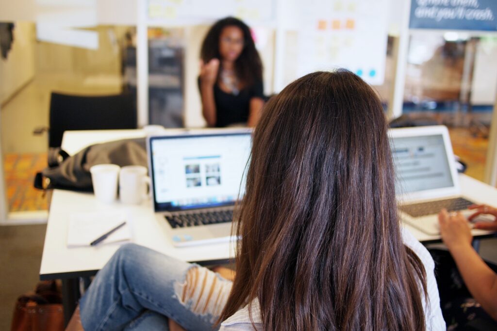 A women sitting in an office desk looking at her laptop PC talking with two others